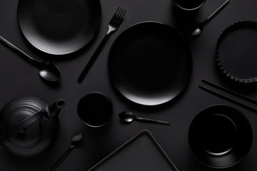 top view of black teapot, plates, bowl, cups, tray, spoons, chopsticks, fork and baking dish on black table - Powered by Adobe