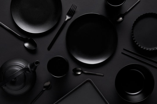 top view of black teapot, plates, bowl, cups, tray, spoons, chopsticks, fork and baking dish on black table