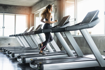 Cute young woman exercising on  treadmill at a gym.Active young woman running on treadmill. smile...