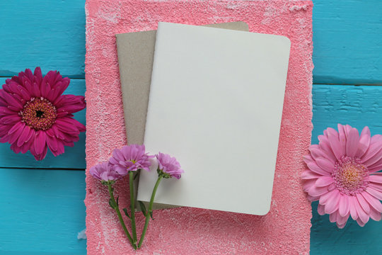empty Notebook and purple daisies on a on a pink square on a bright turquoise wooden background. flat lay. top view, copy space