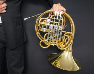 French horn player. Music instrument horn in the hands of hornist. A man in a suit  with a musical instrument. 