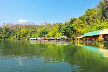 Fototapeta na wymiar View of Wooden house raft floating in Saiyok river kwai at Kanchanaburi Thailand with blue sky and green forest. Beautiful landmark in Asia.