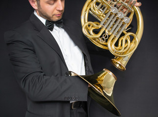 French horn player. Music instrument horn in the hands of hornist. A man in a suit and in a butterfly with a musical instrument. 