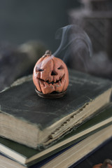 Pumpkin in the form of a skull with smoke from the eyes on old books