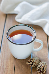 Enameled cup of tea, pine cones and white knitted plaid