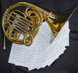 Naklejka premium Musical instrument French horn lies on a black background with notes
