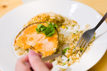 fried sliced salmon with fried rice.man hands use fork and spoon for fusion food.sliced salmon with rice on white plate in restaurant or cafe.man sitting and eating sliced salmon on laptop background