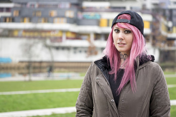 young alternative woman with pink hair standing in front of run-down housing estate                ...