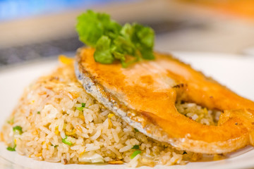 fried sliced salmon with fried rice.man hands use fork and spoon for fusion food.sliced salmon with rice on white plate in restaurant or cafe.man sitting and eating sliced salmon on laptop background