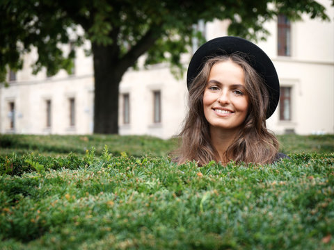 Happy Smiling Young Woman In A Park Looking Over Hedge