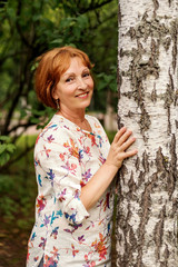 portrait of a middle-aged attractive tranquil woman hugging a birch