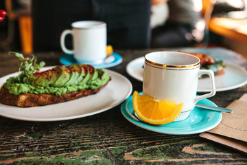 A cup of fresh fragrant tea and next to it a useful and nutritious sandwich with avocado lie on the table. Good morning breakfast