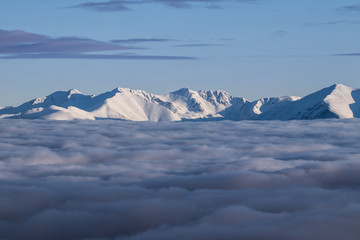 Amazing morning above clouds and fog down in the valley. Snow covered peaks of Tatra mountains peaking through. Feels like flying. Peaceful and relaxing winter vista. Travelling, hiking, adventure.