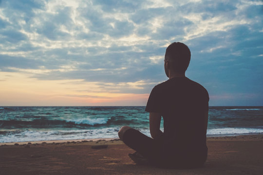 Young Man Meditating On Top Ocean Cliff During Sunset.