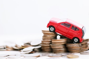 Little red car over a lot of money stacked coins with isolated white background . for loans costs finance concept. empty copy space for text.