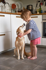 Little girl looking lovingly at her dog while standing in the kitchen