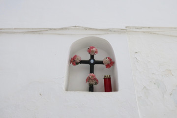 altar in a niche in a white wall with a cross, flowers and a candle