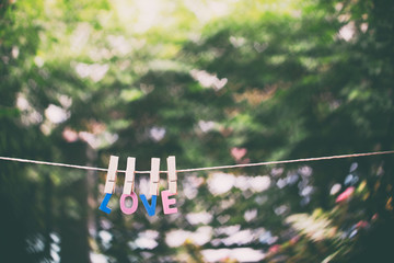 Love word hanging by rope with beautiful  colorful heart bokeh nature background vintage retro tone, Valentines and wedding day greeting card background concept.