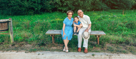 Grandparents and grandson posing for a photo sitting on a bench outdoors