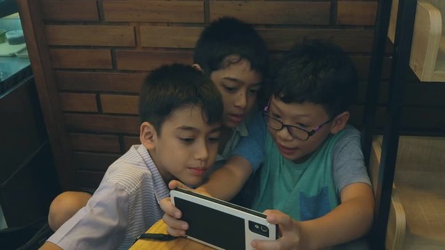 Group of asian boy playing games on mobile phone and tablet computer
