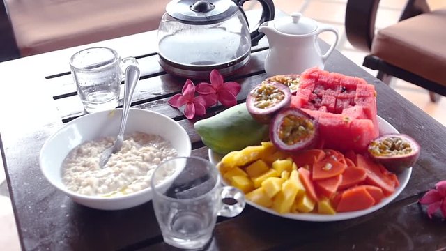 Delicious and nutritious breakfast in the early morning with porridge and tropical fruits of mango, papaya, passion fruit and watermelon. Slow motion, HD, 1920x1080