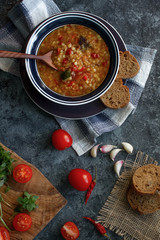 Delicious homemade soup from organic red lentil, vegetables, basil, garlic and piece of black bread on dark stone table. Healthy lifestyle, vegeterian food concept, top view, selective focus