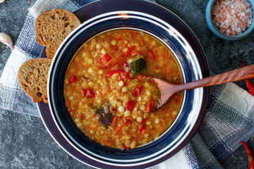 Delicious homemade soup from organic red lentil, vegetables, basil, garlic and piece of black bread on dark stone table. Healthy lifestyle, vegeterian food concept, top view, selective focus