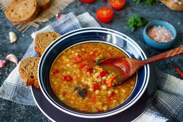 Delicious homemade soup from organic red lentil, vegetables, basil, garlic and piece of black bread on dark stone table. Healthy lifestyle, vegeterian food concept, selective focus