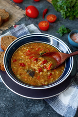 Delicious homemade soup from organic red lentil, vegetables, basil, garlic and piece of black bread on dark stone table. Healthy lifestyle, vegeterian food concept, selective focus