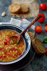 Delicious homemade soup from organic red lentil, vegetables, basil, garlic and piece of black bread on dark stone table. Healthy lifestyle, vegeterian food concept, selective focus
