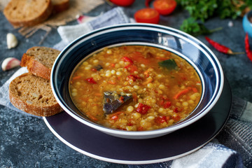 Delicious homemade soup from organic red lentil, vegetables, basil, garlic and piece of black bread on dark stone table. Healthy lifestyle, vegeterian food concept, selective focus