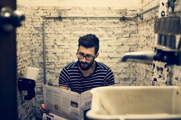 Man in a restroom reading newspaper - obrazy, fototapety, plakaty