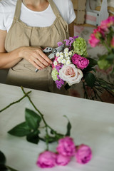 woman florist making bouquet of pink flowers indoor. Female florist preparing bouquet of roses in flower shop. entrepreneurship, small business, workplace concept 