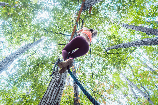 Very fit and athletic woman climbing a rope tied to a tree