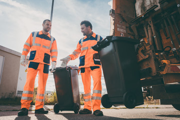 Garbage removal men working for a public utility emptying trash container