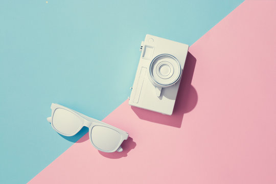 Creative Layout Made Of Painted Camera And Sunglasses On Pastel Pink And Blue Background. Minimal Summer Exotic Concept With Copy Space.