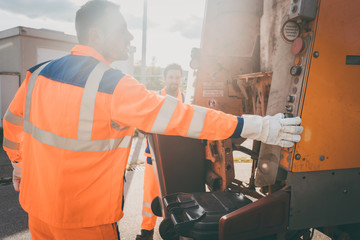 Two refuse collection workers loading garbage into waste truck emptying containers