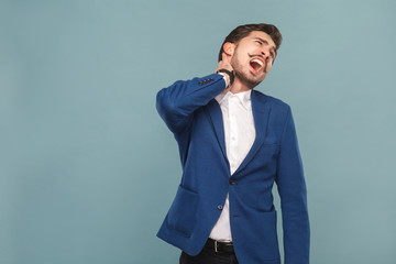 Man shout because pain in neck. portrait of handsome bearded businessman in blue suit and white shirt, with smart watch. Indoor studio shot, isolated on light blue background