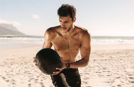 Man training at the beach using a medicine ball - Powered by Adobe