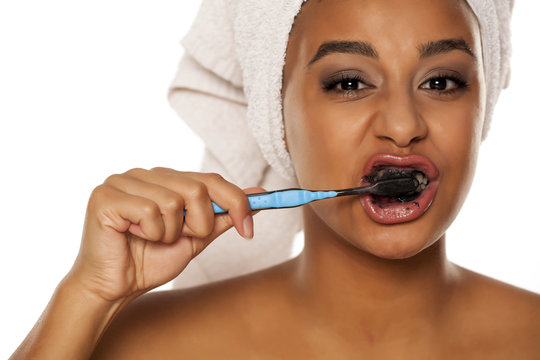 portrait of a happy young dark-skinned woman brushing her teeth with black toothpaste on a white background