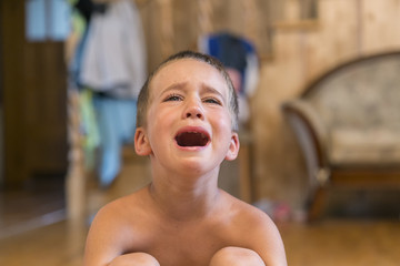 Little boy sitting on the floor, he's upset and crying. The child is crying sitting on the floor in the room.