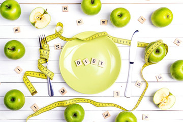 Diet concept table setting with cutlery, yellow measuring tape and green apples on white wooden...