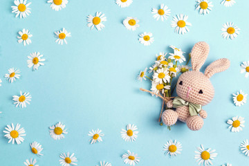 Cute toy bunny with chamomile flowers and copy space on a blue background.