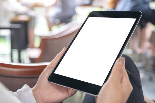 Mockup image of hands holding black tablet pc with white blank desktop screen in cafe
