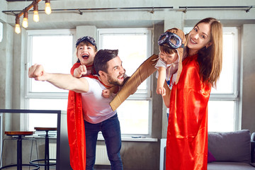 Happy family in superhero costumes playing together in a room.