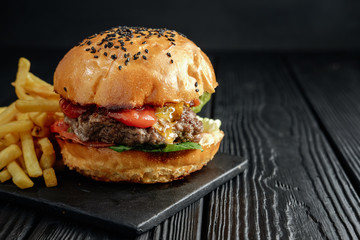 homemade  juicy burger on dark wooden board with French fries. Street food, fast food.
