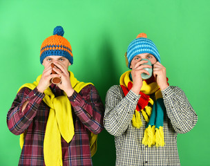 Twin brothers wearing warm hats and scarves hold cups