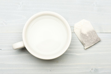 Mug filled with boiling water and teabag on white background. Process of tea brewing in ceramic mug, top view. Cup or white porcelain mug with transparent hot water and bag of tea. Tea time concept