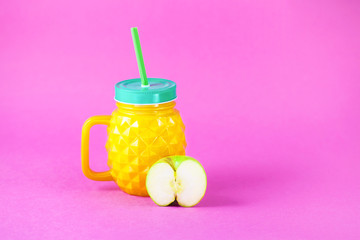 a bottle of pineapple with juice and a piece of apple on a bright rose background Copy space
