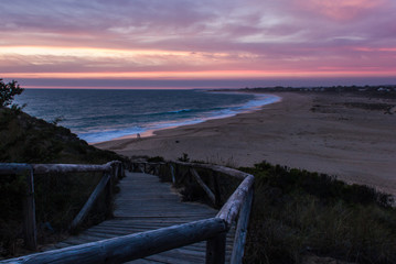Fototapeta premium Drewniana promenada prowadząca w dół do pustej plaży Zahora o ładnym zachodzie słońca w Kadyksie w Hiszpanii. Wspaniały zmierzch nad morzem w Andaluzji. Letnie wakacje, koncepcje turystyczne